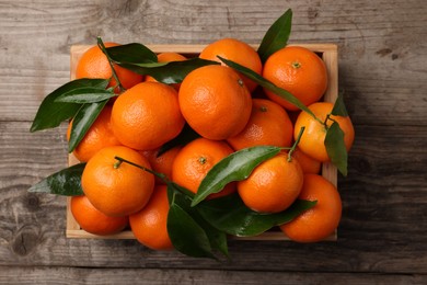 Photo of Delicious tangerines with leaves in crate on wooden table, top view