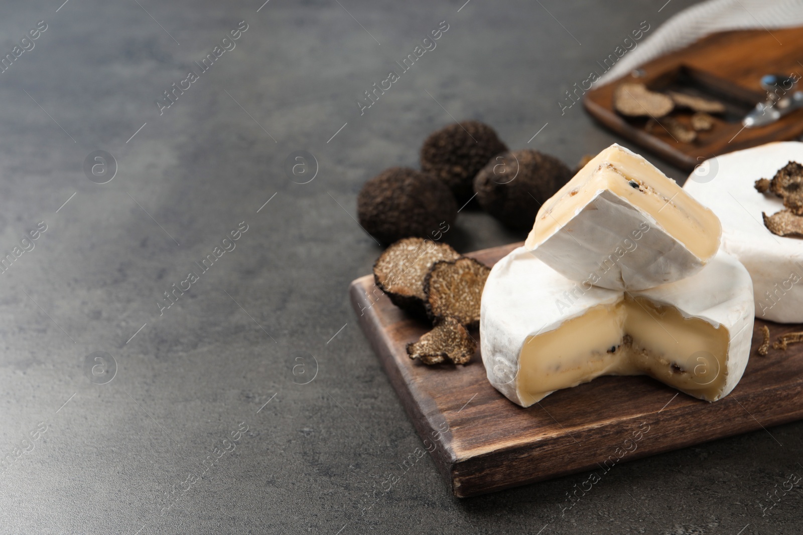 Photo of Wooden board with delicious truffle cheese on grey table. Space for text