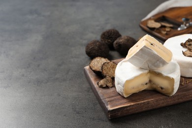 Photo of Wooden board with delicious truffle cheese on grey table. Space for text