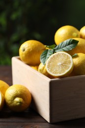 Photo of Fresh lemons in crate on wooden table, closeup