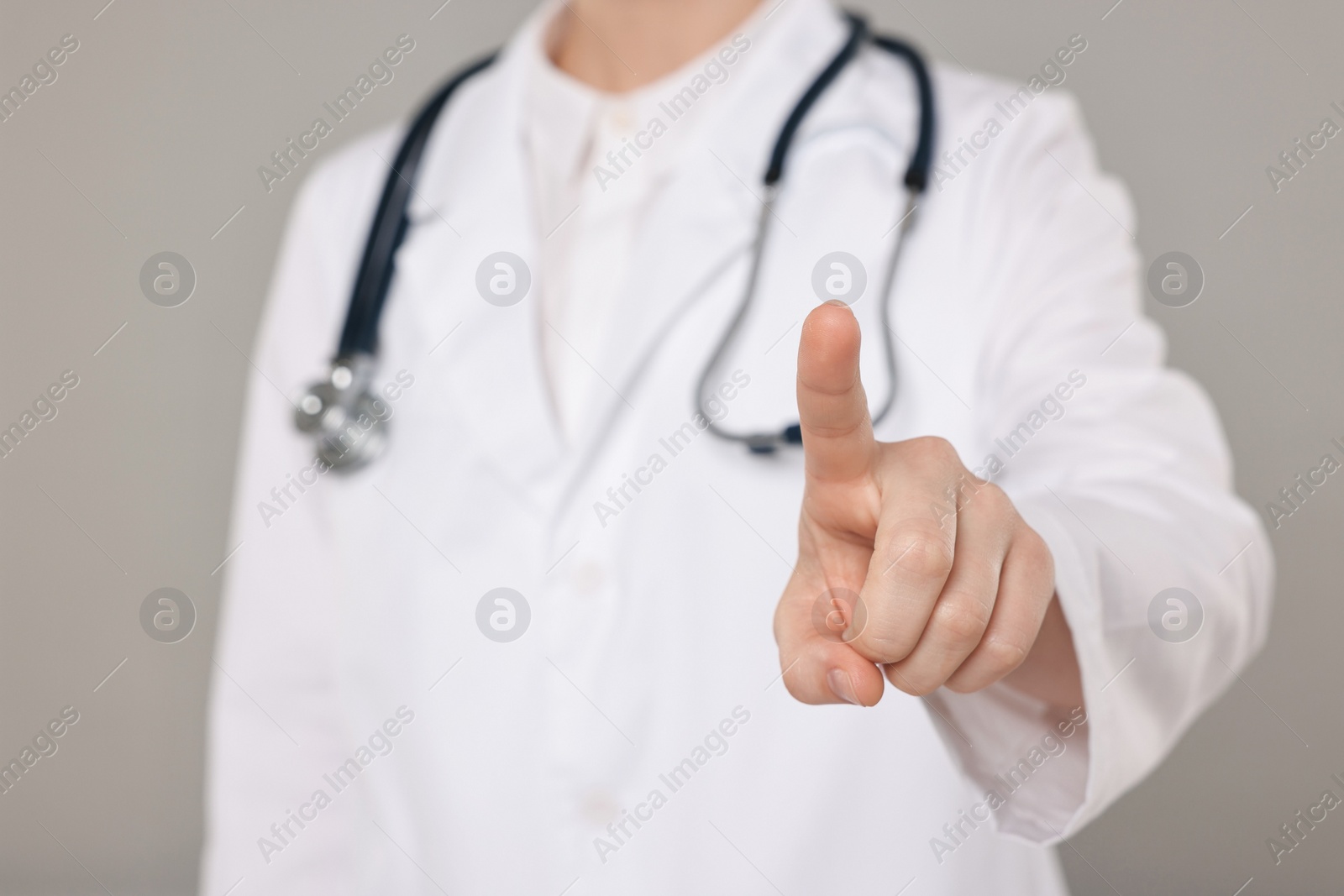 Photo of Doctor with stethoscope pointing on grey background, closeup