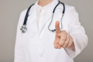 Photo of Doctor with stethoscope pointing on grey background, closeup