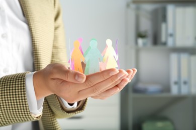 Photo of Woman holding paper human figures on blurred background, closeup. Diversity and inclusion concept