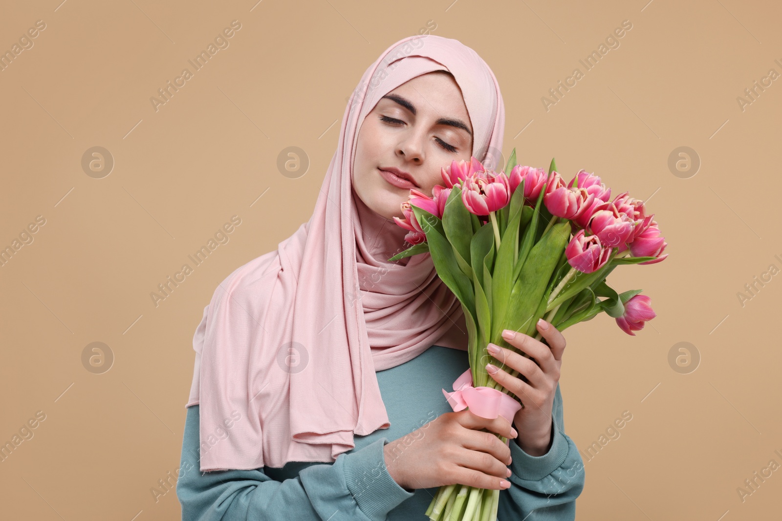 Photo of Happy woman in hijab with beautiful bouquet on beige background