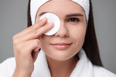 Photo of Young woman cleaning her face with cotton pad on grey background, closeup