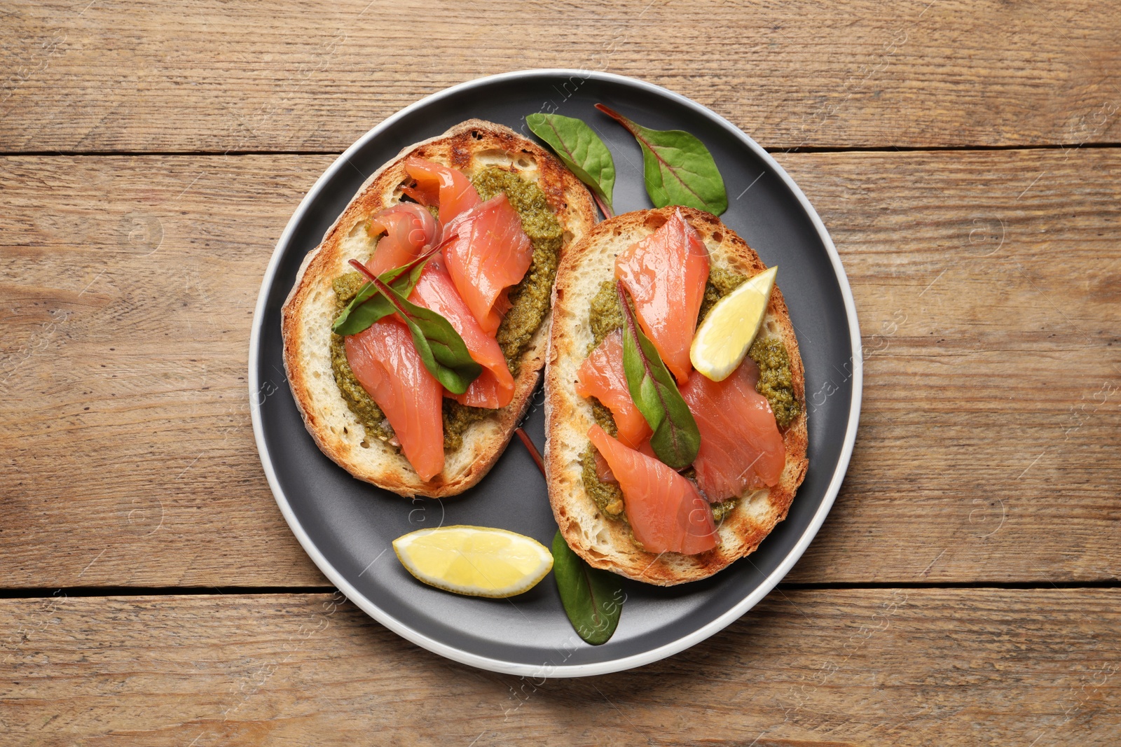 Photo of Delicious bruschettas with salmon and pesto sauce on wooden table, top view