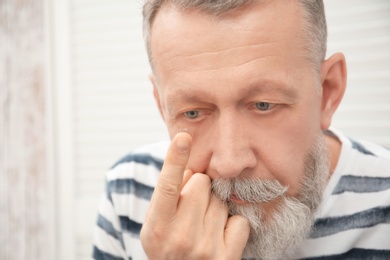 Photo of Senior man putting contact lens in his eye indoors