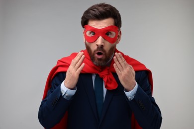 Photo of Surprised businessman wearing red superhero cape and mask on beige background