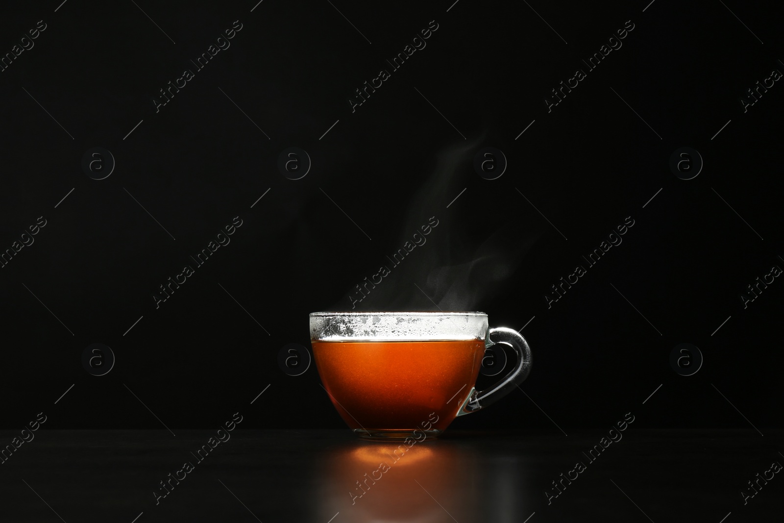 Photo of Glass cup of hot tea on table against black background, space for text