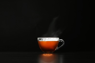 Photo of Glass cup of hot tea on table against black background, space for text