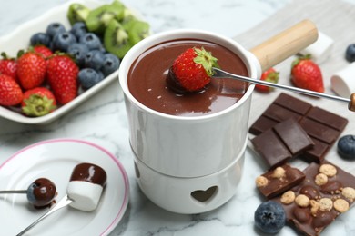 Photo of Dipping fresh strawberry in fondue pot with melted chocolate at white marble table