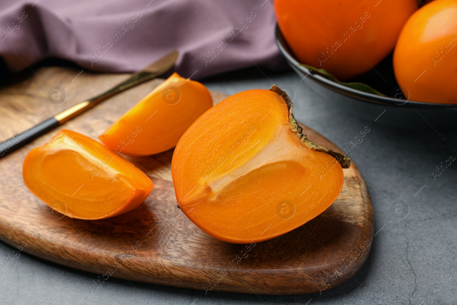 Photo of Pieces of delicious ripe persimmons and knife on wooden board, closeup