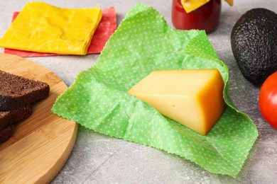 Photo of Piece of cheese in beeswax food wrap on light grey table