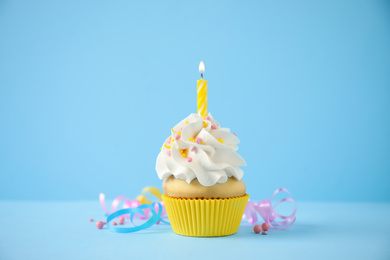 Photo of Delicious birthday cupcake with candle on light blue background