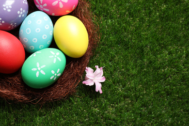 Photo of Colorful Easter eggs in decorative nest on green grass, closeup. Space for text