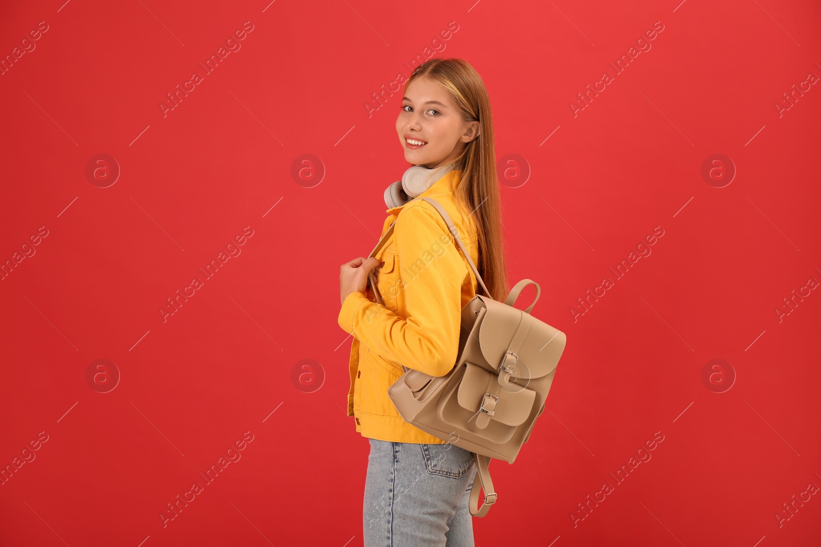 Photo of Teenage student with backpack and headphones on red background