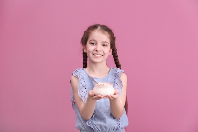 Cute girl eating tasty yogurt on color background