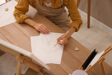Photo of Young woman drawing female portrait at table indoors, above view