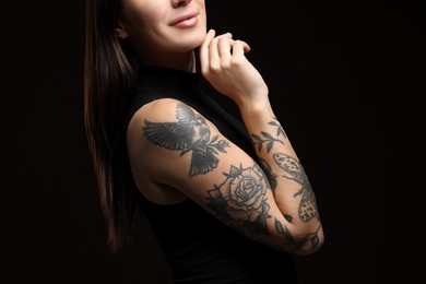 Photo of Woman with tattoos on arm against black background, closeup