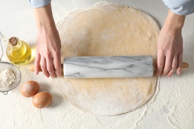 Woman rolling raw dough at table, top view