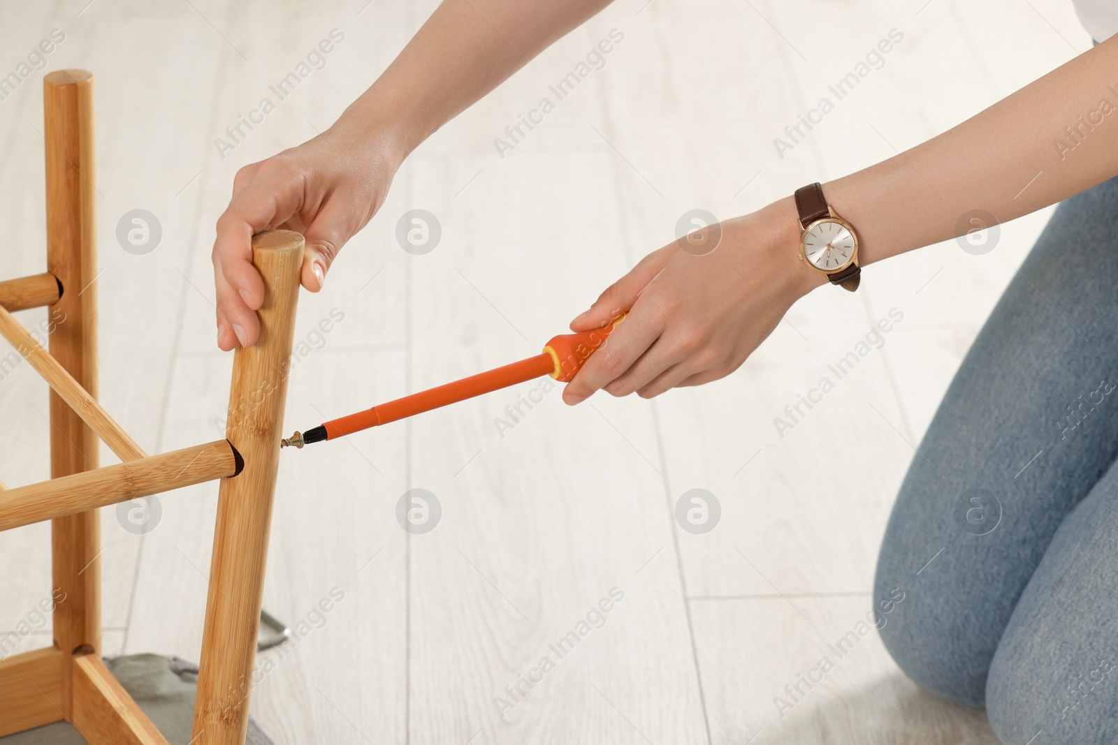 Photo of Woman with screwdriver assembling furniture on floor, closeup