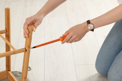 Photo of Woman with screwdriver assembling furniture on floor, closeup