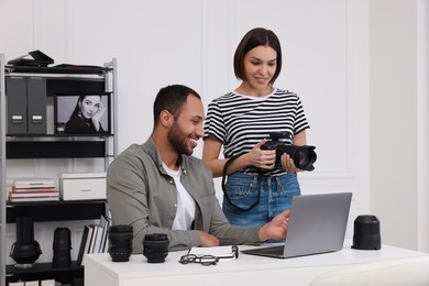Photo of Young professional photographers with camera working on laptop in modern photo studio