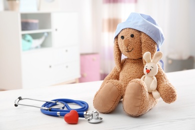 Photo of Composition with toy bunnies, stethoscope and heart on table indoors, space for text. Children's doctor