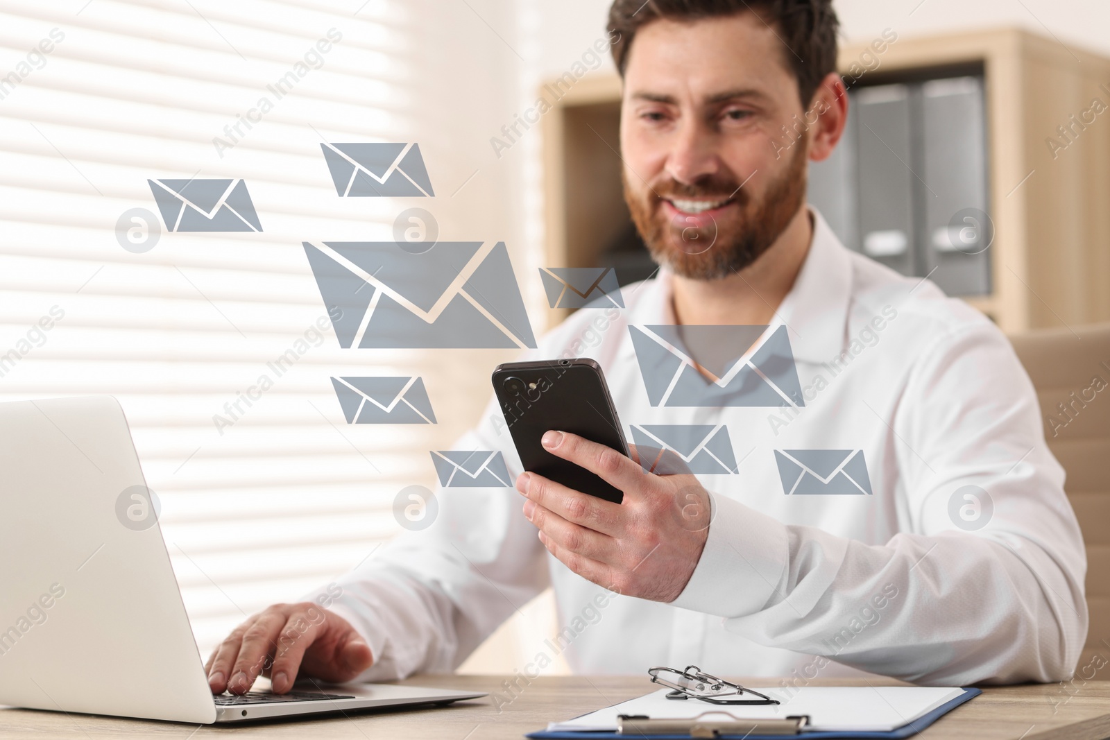 Image of Smiling man with smartphone chatting at table in office. Many illustrations of envelope as incoming messages around device