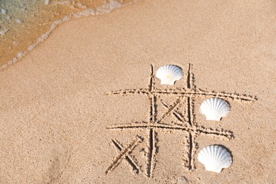 Playing Tic tac toe game with shells on sand near sea, above view. Space for text