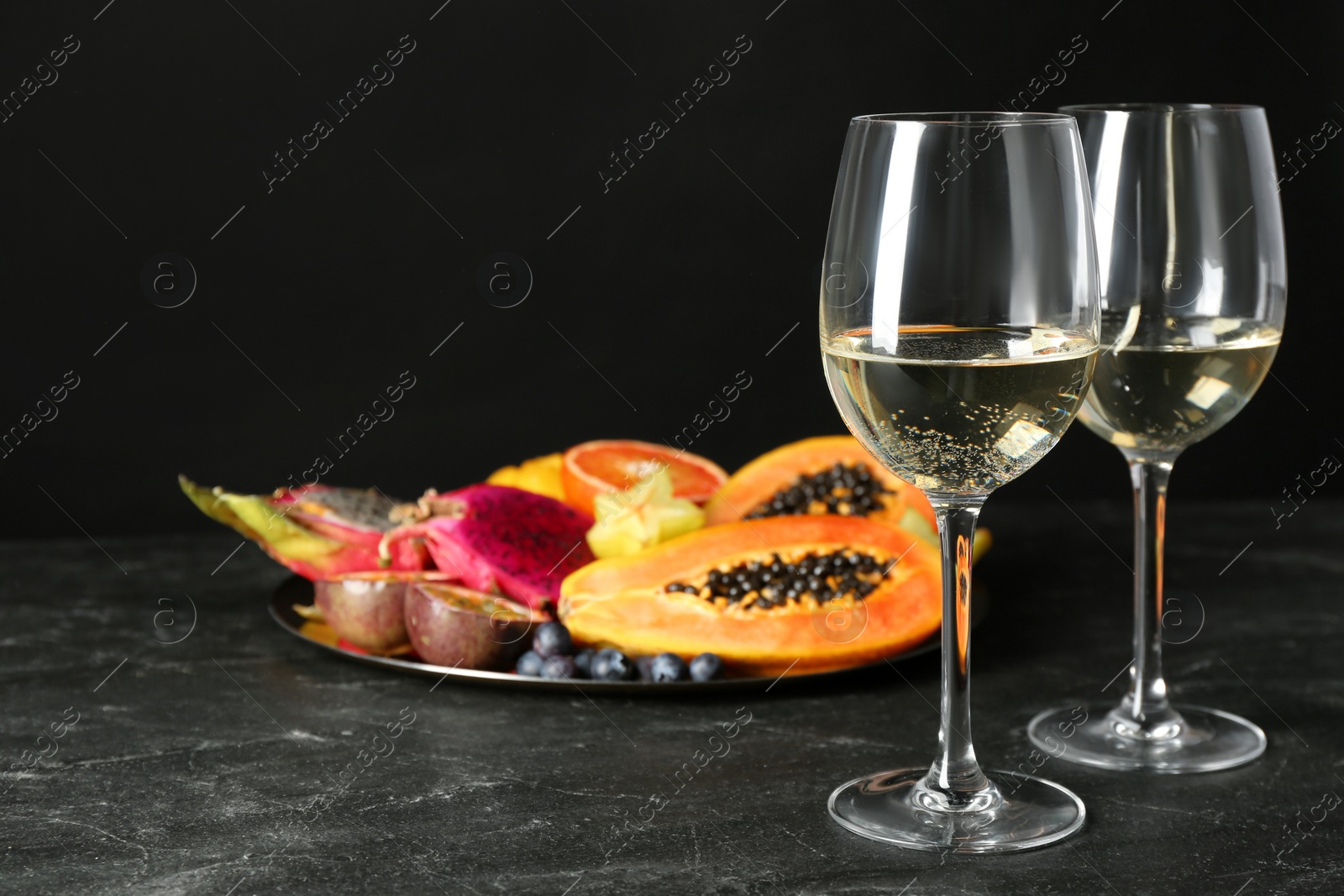 Photo of Delicious exotic fruits and wine on black table, space for text