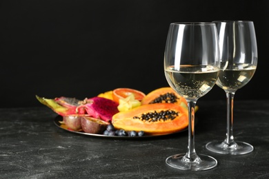 Photo of Delicious exotic fruits and wine on black table, space for text