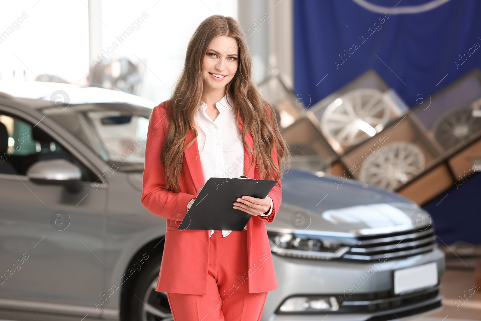 Photo of Young saleswoman with clipboard in car dealership