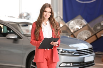 Young saleswoman with clipboard in car dealership