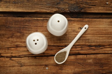 White ceramic salt and pepper shakers with spoon on wooden table, flat lay