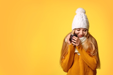 Portrait of young woman in stylish hat and sweater with paper coffee cup on color background, space for text. Winter atmosphere