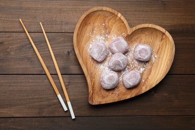 Photo of Heart shaped plate with delicious mochi and chopsticks on wooden table, flat lay. Traditional Japanese dessert
