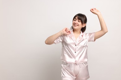 Happy woman in pyjama on light grey background, space for text