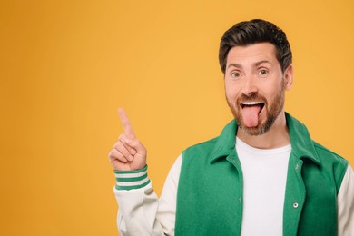 Photo of Man showing his tongue and pointing at something on orange background, space for text