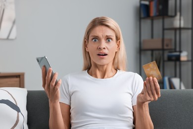 Scared woman with credit card and smartphone on sofa at home. Be careful - fraud