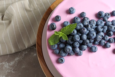 Photo of Wooden stand with tasty blueberry cake on grey table, top view