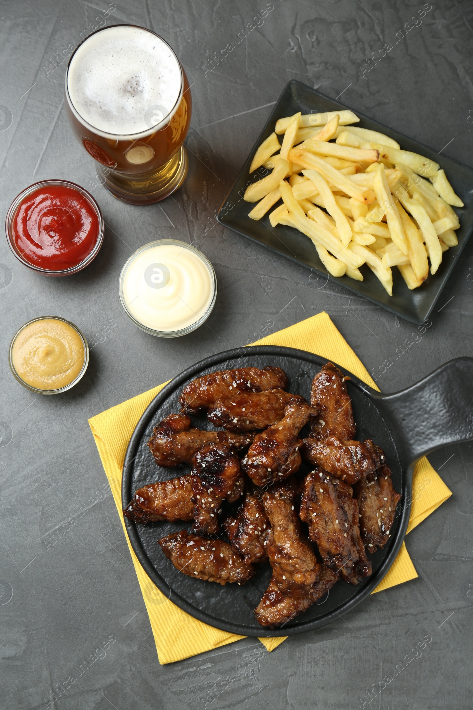 Photo of Tasty roasted chicken wings, sauces, french fries and glass of beer on black table, flat lay