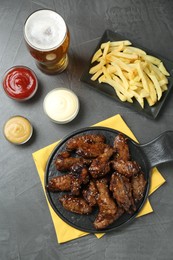 Tasty roasted chicken wings, sauces, french fries and glass of beer on black table, flat lay