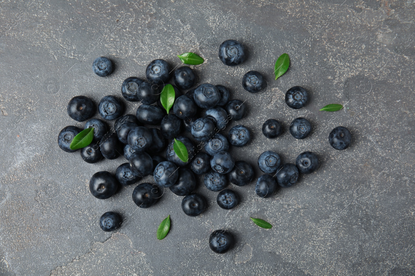 Photo of Pile of tasty fresh blueberries and leaves on grey stone background, top view