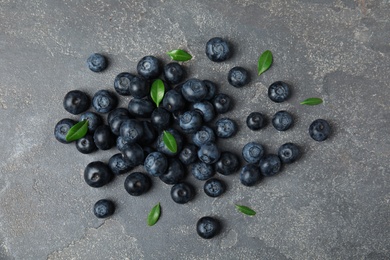 Pile of tasty fresh blueberries and leaves on grey stone background, top view