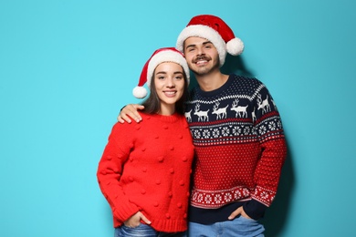 Photo of Young couple in warm sweaters and Christmas hats on color background