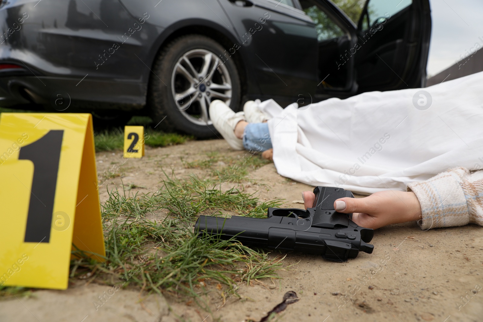 Photo of Crime scene with dead woman's body, gun and markers outdoors, closeup