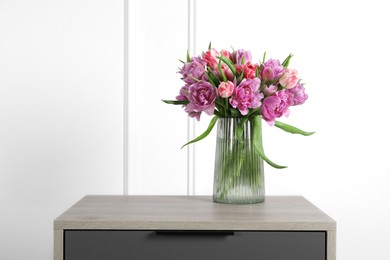 Photo of Beautiful bouquet of colorful tulip flowers in vase on wooden bedside table