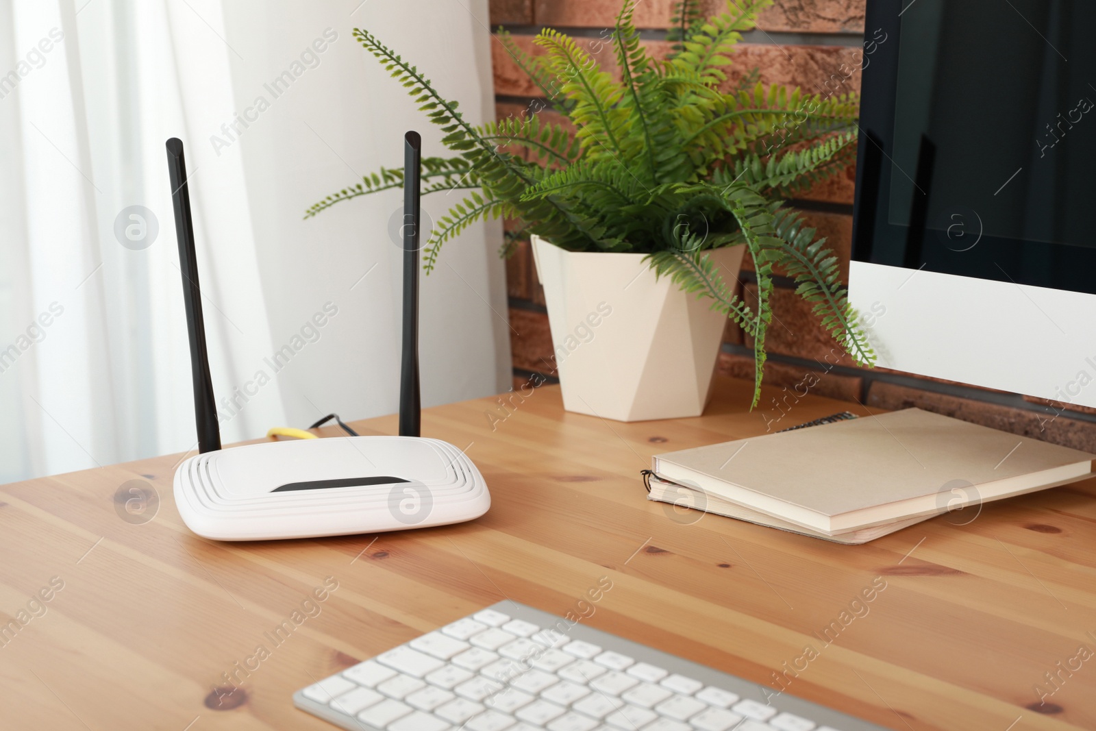 Photo of Modern wi-fi router near computer on wooden table