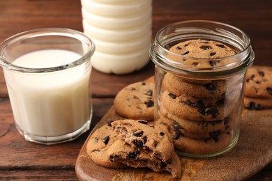Photo of Glass jar with delicious chocolate chip cookies and milk on wooden table, closeup